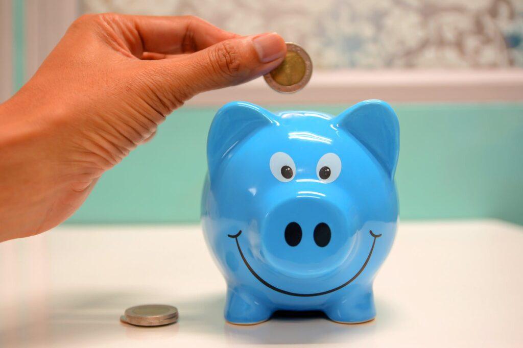 Main déposant une pièce dans une tirelire bleue, illustration du capital accumulé pour la retraite