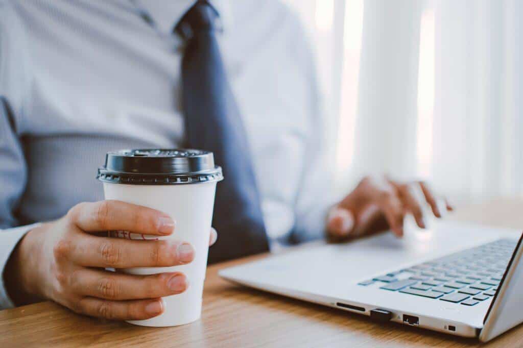 Travailleur indépendant en chemise devant son ordinateur portable, une boisson à la main